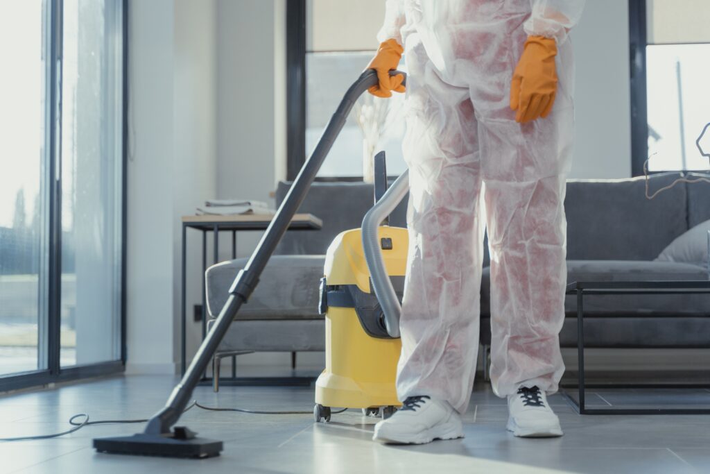 pexels-photo-6195951-6195951 A cleaner in protective coveralls and gloves vacuuming a modern living room.